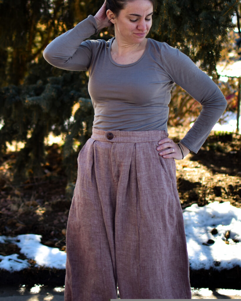 white woman dressed in nutmeg linen twill high waisted wide legged arthur pants and gray shirt. she is touching her hair