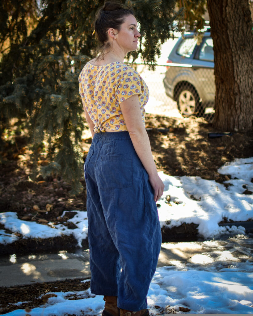 white woman in blue linen high waisted wide legged pants and yellow floral print crop top looking off into the distance