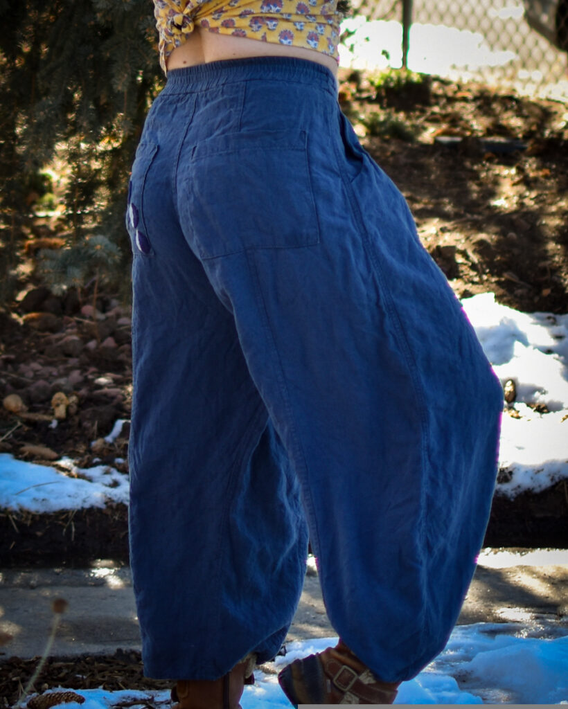 white woman in blue linen high waisted wide-legged arthur pants facing to the side with one legged raised