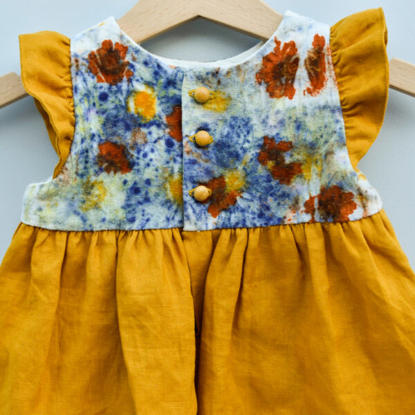 close up of back of toddler dress with naturally dyed bodice using eco-printing technique with images of flowers on raw silk, golden gathered skirt and arm ruffles