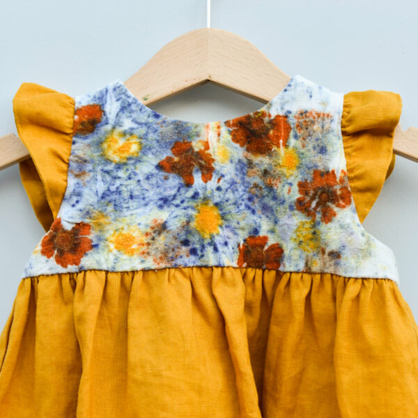 detail of top of toddler dress with naturally dyed bodice using eco-printing technique with images of flowers on raw silk, golden gathered skirt and arm ruffles