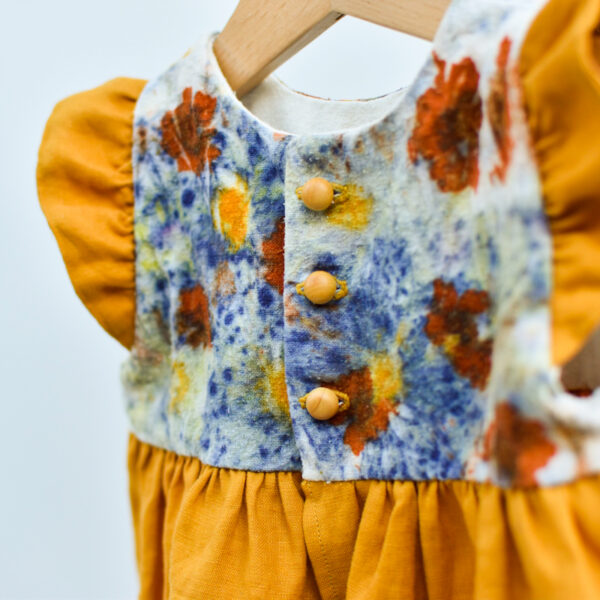 close up of back of toddler dress with naturally dyed bodice using eco-printing technique with images of flowers on raw silk, golden gathered skirt and arm ruffles. Detail of 3 wooden buttons