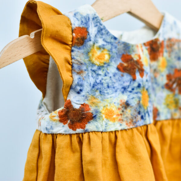 detail of top of toddler dress with naturally dyed bodice using eco-printing technique with images of flowers on raw silk, golden gathered skirt and arm ruffles