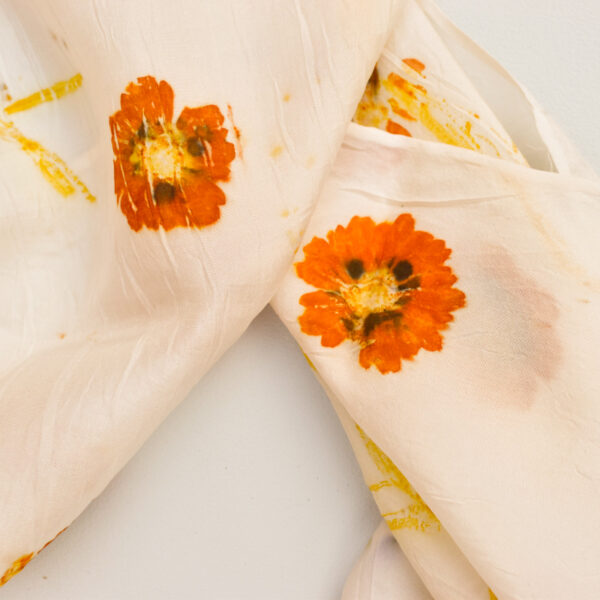 detail of coreopsis orange flower and yellow stem on white background of folded silk