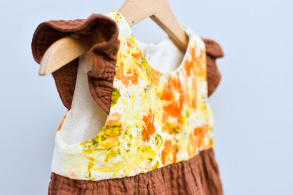 detail of 2T toddler dress, sleevless with ruffles, high waist, gathered skirt. bodice is naturally dyed with flowers showing images of sulfur cosmos and marigold petals. skirt and ruffles are double gauze cotton with checked texture