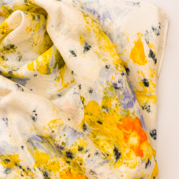 close up of rumpled silk scarf with yellow, orange, and light and dark purple flower and petal images printed onto white background