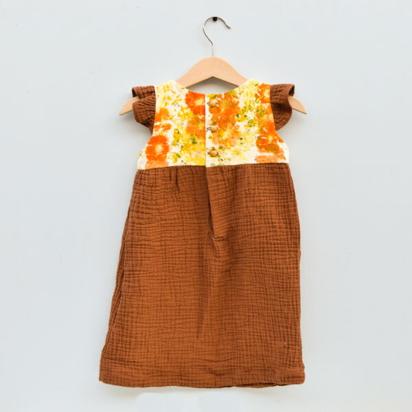 back of 2T toddler dress, sleevless with ruffles, high waist, gathered skirt. bodice is naturally dyed with flowers showing images of sulfur cosmos and marigold petals. skirt and ruffles are brown double gauze cotton with checked texture . 3 round wooden buttons make the closure with half-placket into skirt