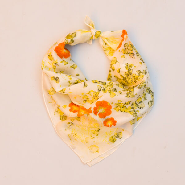 silk scarf tied into bandana with images of orange sulfur cosmos flowers and marigold petals with black flecks of yellow scattered on white background
