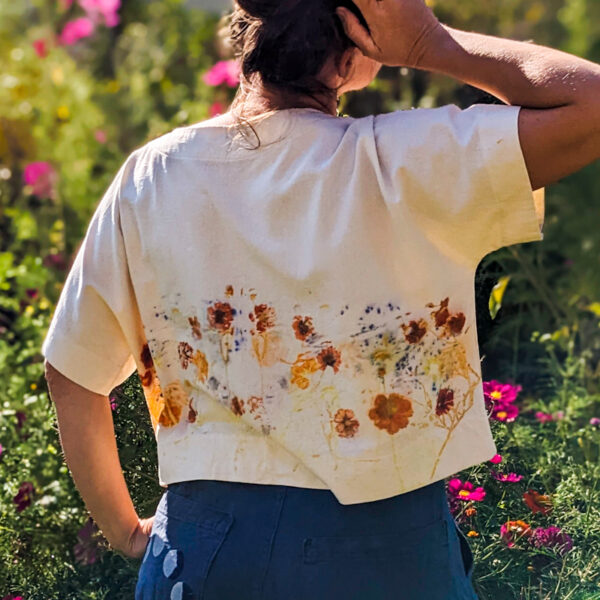 cropped picture woman modeling loose fitting boxy-tee with earthy images of flowers. Orange tones and purple with green backdrop